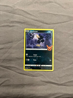 Pokémonkort Murkrow med Pikachu-sticker - Säljer ett Pokémonkort med Murkrow-motiv. Kortet har en gul ram, mörkblå bakgrund och en bild på Murkrow i en nattlig miljö. Det finns även en orange Pikachu-sticker på framsidan. Perfekt för samlare eller Pokémon-fans.