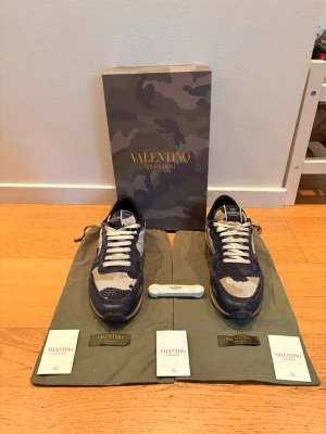 Valentino rockrunners - Snygga sneakers från Valentino Garavani med camomönster i blått, vitt och beige. Skorna har vita snören, svart sula och detaljer i mocka och mesh. Kommer med originalkartong, dustbags, certifikat och skosnören. Det finns en defekt som syns på sista bilden. De är äkta och hör av er vid minsta fundering!
