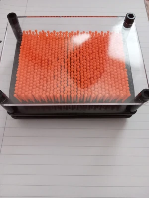 Leksak - Rolig pin leksak med orange plastpinnar och svart ram. Perfekt för att skapa 3D-former genom att trycka olika objekt mot pinnarna. Leksaken har en rektangulär form och genomskinlig framsida. Den är använd men detta syns knappt. Köptes på Flying Tiger. 