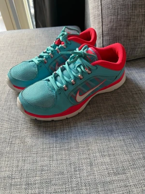 Turkosa Nike sneakers storlek 37,5 - Snygga turkosa Nike sneakers med mesh och syntetmaterial. Storlek 37,5. Skorna har vit sula vilket gör att de passar för inomhusträning. Men kan såklart även användas som vanliga sneakers i vardagen. 