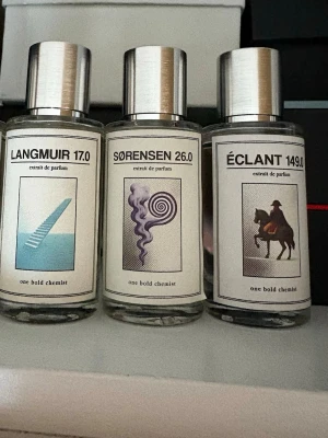 Parfymflaskor från One Bold Chemist - Tre parfymflaskor från One Bold Chemist: Langmuir 17.0, Sørensen 26.0 och Éclant 149.0. Flaskorna är transparenta med silverfärgade lock och har unika grafiska etiketter i vitt med motiv som trappa, spiral och ryttare. Perfekt för dig som gillar stilrena och kreativa doftflaskor.