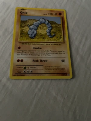 Onix Pokémonkort Base Set - Onix Pokémonkort från Base Set med gul ram och klassisk design. Kortet har Onix-illustration mot en naturbakgrund och visar attackerna Harden och Rock Throw. Text och detaljer på engelska. Perfekt för samlare eller Pokémonfans.