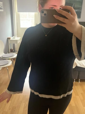 Svart stickad tröja med vida ärmar - Säljer en svart stickad tröja med vida ärmar och vita ribbade kanter vid ärmslut och nederkant. I storlek M men har krympt lite i tvätten😇
