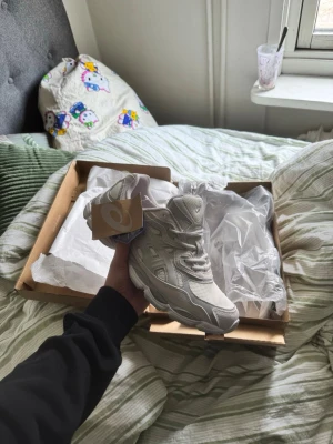 Asic gel nyc cloud gray storlek 43,5 - Säljer ett par vita Asics Gel sneakers med mesh och syntetmaterial. Skorna har en chunky sula och klassisk Asics-logga på sidan. Perfekt för dig som gillar sportig och clean stil. Skorna har snörning och låg profil.