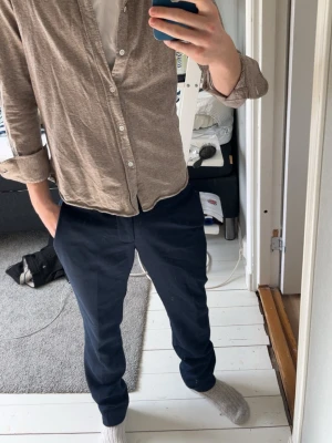 Beige skjorta i bomull med knappar - Snygg beige skjorta i mjukt bomullstyg med klassisk krage och vita knappar framtill. Skjortan har lång ärm och en avslappnad passform, perfekt att bära öppen över en t-shirt. Enkel och stilren design utan mönster eller extra detaljer.