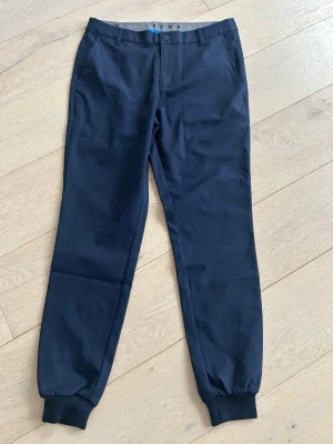 Mörkblåa golfbyxor från Puma - Snygga mörkblå golfbyxor från Puma med avsmalnande ben och muddar vid anklarna. Klassisk design med bälteshällor, sidofickor och bakfickor. Perfekta för en sportig och avslappnad stil. Tillverkade i ett mjukt och bekvämt material. Hör av er vid fler frågor, priset går att diskutera.