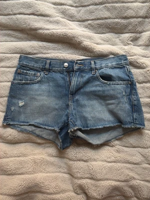 Blå jeansshorts från Perfect Jeans - Säljer ett par blå jeansshorts från Perfect Jeans i storlek 36. De har råa kanter, klassisk femficksdesign och slitna detaljer framtill. Perfekta för varma dagar och en avslappnad stil.