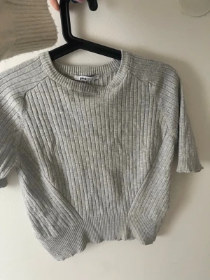 Grå ribbad stickad topp Gina Tricot - Snygg grå ribbad stickad topp från Gina Tricot med rund halsringning och korta ärmar. Storlek L men passar S🩷