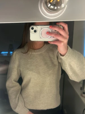 Beige stickad tröja med puffärm - Mysig beige stickad tröja med rund halsringning och diskreta puffärmar. Tröjan har ribbstickade muddar vid ärmslut och nederkant. Perfekt för kalla dagar och enkel att matcha med olika outfits.