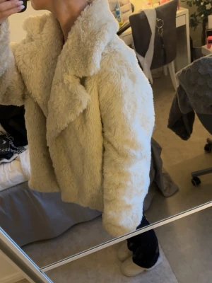Beige teddyjacka med stor krage - Supermysig och snygg teddyjacka i storlek L! Jackan är fluffig och har knäppning framtill. Perfekt för att hålla sig varm och snygg under kyliga dagar.