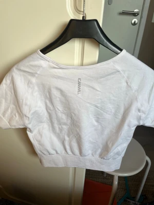 Vit croppad topp från ICANIWILL - Säljer en vit croppad topp från ICANIWILL med korta ärmar och bred resår i midjan. Toppen har en enkel och sportig design med logga på bröstet och är perfekt för träning eller chill. Materialet känns mjukt och stretchigt. Men den har en kaffefläck på magen men den går säkert att bleka bort om man vill.