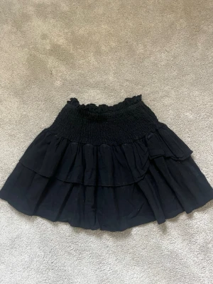 Svart volangkjol med smock - Supersöt svart kjol med bred smock i midjan och dubbla volanger. Den är ifrån SHEIN och är i storlek 130