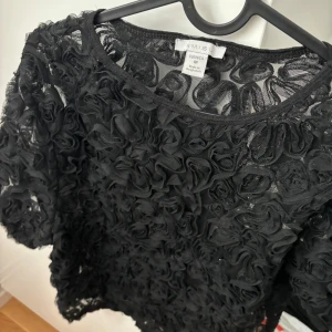 Svart blommig topp från New Yorker - Snygg svart topp från Amisu med 3D-blommor över hela tyget. Toppen är kortärmad.