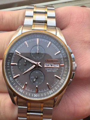 Champion Spider Sport Klocka/Watch -  Champion Spider Sport kronografklocka med safirglas och 10 ATM vattentålighet. Boetten är i rostfritt stål och har en tvåfärgad länk i stål och guldton. Urtavlan är grå med tre sub-urtavlor och datumvisning. Klockan har ett kvartsurverk.  Champion Spider Sport med safirglas och 10 ATM vattentålighet. Boetten är i rostfritt stål och har en tvåfärgad länk i stål och guldton. Urtavlan är grå med tre sub-urtavlor och datumvisning.