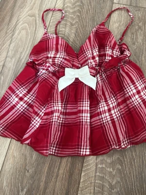 Rött rutigt nattlinne från Gina Tricot - Supersött nattlinne från Gina Tricot i rött och vitt rutigt mönster. Modellen har tunna axelband, v-ringning och en stor vit rosett framtill. Materialet är lätt och luftigt, perfekt för mysiga kvällar hemma.