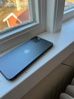 iPhone 11 Pro rymdgrå 256GB - Snygg iPhone 11 Pro i rymdgrå färg med elegant glasbaksida och rostfri ram. Telefonen har trippelkamera på baksidan och Apple-loggan centrerad. Perfekt för dig som vill ha en kraftfull och stilren mobil med premiumkänsla.