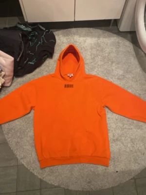 Orange hoodie från Weekday - Säljer en orange hoodie från Weekday med svart streckkodstryck och årtalen 1989 och 1994 på bröstet. Hoodien har klassisk känguruficka och ribbade muddar. Perfekt för dig som gillar streetwear och vill sticka ut med färg.