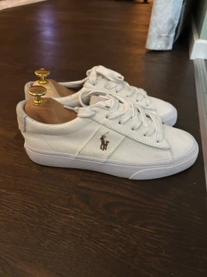 Vita sneakers från Polo Ralph Lauren - Är i nyskick. Har använts en gång och har små fläckar på inre sidan av ena skon, se om sista bilden. Men inga fler fläckar eller skador. Dom har bara använts en gång. Nypris 1300
