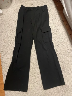 Svarta cargobyxor med raka ben - Säljer ett par svarta cargobyxor med raka ben och stora fickor på sidorna. Byxorna har bälteshällor. 