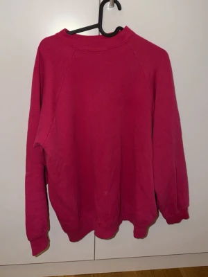 Mörkrosa sweatshirt utan huva - En enkel och stilren mörkrosa sweatshirt med rund halsringning och långa ärmar. Tröjan har ribbade muddar vid ärmslut och nederkant. Perfekt för en avslappnad och bekväm look. Materialet känns mjukt och skönt mot huden.