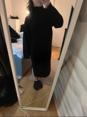 Svart stickad långklänning med slits - Mysig svart stickad långklänning med polokrage och lång ärm. Klänningen har en snygg slits på sidan. Perfekt för dig som gillar en avslappnad men ändå stilren look.