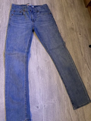 Levi's blå slim fit jeans - Klassiska blå jeans från Levi's i slim fit-modell med fem fickor och dragkedjegylf. Jeansen har en snygg mellanblå tvätt och är tillverkade i bomull med en liten stretch för extra komfort. Perfekta för en avslappnad och trendig look.