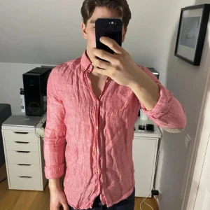 Rosa linneskjorta från Massimo dutti - Säljer en snygg rosa skjorta från Massimo dutti i linne med klassisk krage och knappar framtill. Skjortan har långärmad design och diskreta beige armbågslappar som ger en cool detalj. Perfekt för dig som gillar stilrena plagg med lite edge.