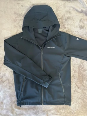 Svart vindjacka från Peak Performance - Snygg svart vindjacka från Peak Performance. Riktigt snygg och bra nu till våren. Litet hål i högra fickan. Nypris 2.200kr. 