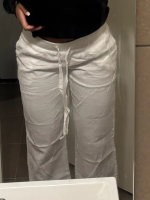 Alobha Vita linnebyxor med - Säljer ett par vita linnebyxor med avslappnad passform och dragsko i midjan. Byxorna är raka i modellen och tillverkade i ett lätt och luftigt linnematerial, perfekta för en chill och stilren look.