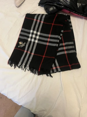 Burberry svart rutig halsduk - Svart halsduk från Burberry med klassiskt rutmönster i grått, vitt och rött. 