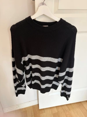 Svart stickad tröja med ränder Nelly - Säljer en svart stickad tröja från Nelly med breda horisontella grå ränder. Tröjan har rund halsringning och långa ärmar. Perfekt för dig som gillar en avslappnad och trendig look med klassiska färger.