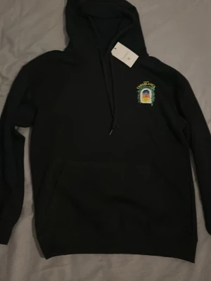 Svart hoodie från Casablanca - Snygg svart hoodie från Casablanca med trycket 'Avenida Casablanca' och ett färgglatt fönstermotiv på bröstet. Klassisk känguruficka framtill och justerbar huva med snören. Perfekt för dig som vill ha en stilren men unik hoodie.