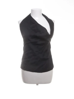 Svart omlott halterneck-top - Snygg svart halterneck-top med omlott-design och knytning i ryggen. Toppen har en djup v-ringning och är ärmlös, vilket ger en stilren och trendig look. Perfekt att styla med jeans eller kjol för en cool outfit. Helt oanvänd och prislappen är kvar.