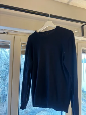 Mörkblå stickad tröja Massimo Dutti - Snygg mörkblå stickad tröja från Massimo Dutti i en klassisk modell med rund halsringning. Tillverkad i 100% extra fin merinoull för en mjuk och skön känsla. Perfekt att matcha med jeans eller chinos. Som visas på bild så är det ett mindre hål i armhålan som gör att fixa.