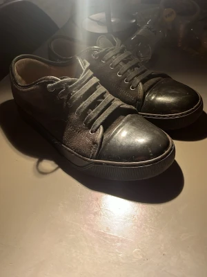 Svarta sneakers från Lanvin - Snygga svarta sneakers från Lanvin med klassisk låg profil. Skorna har en mix av mocka och läder, rund tå och matchande svarta skosnören. Perfekta för dig som gillar stilrena och exklusiva sneakers med en lyxig känsla.