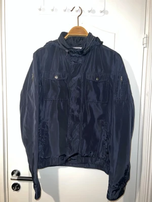 Mörkblå vindjacka - Polo Saint Vincent jacka i mörkblå färg, storlek S. Jackan är i jättebra skick och sparsamt använd. Har huva som kan vikas in i kragen, så jackan kan användas både med och utan huva, vilket syns på bilderna. Passar perfekt för höst, vår och mild vinter. Finns att hämta i Södertälje eller Örebro.