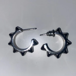 Silvriga Edblad peak örhängen med nitar - Coola silvriga örhängen i ringmodell med utstickande nitar runt om. Perfekt accessoar för dig som gillar en edgy och alternativ stil. Metallisk finish och robust design som sticker ut.