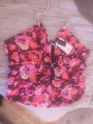 Blommig glittrig linnetopp med strassband - Supersnygg linnetopp från Bik Bok med färgglatt blommönster i rosa, rött och lila. Toppen har glittriga strassband som knyts runt nacken  och en liten snörningsdetalj framtill. Perfekt för dig som vill sticka ut och addera lite extra bling till outfiten.