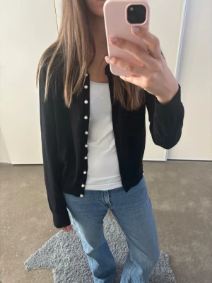 Svart kofta med pärlknappar - Stilren svart kofta med långa ärmar från HM. Passar dig som har storlek S/M