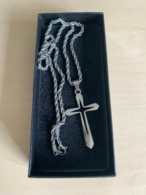 Ropechain halsband 50cm med kors i rostfritt stål - Snyggt halsband i metall med ett blankt kors som hänge. Kedjan har tvinnad design och ett robust lås. Perfekt accessoar för dig som gillar stilrena och klassiska smycken med en modern touch.