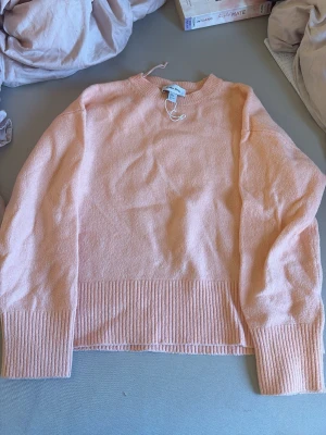korall stickad tröja - Mysig persikofärgad stickad tröja från & Other Stories. Tröjan har rund hals, långa ärmar och breda ribbade muddar vid ärmslut och nederkant. Perfekt för lager-på-lager och enkel att matcha med jeans eller kjol.