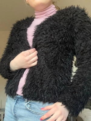 Svart fluffig cardiganjacka/festjacka - Säljer en svart, superfluffig cardiganjacka med lång ärm och öppen front. Jackan har en cool, lurvig textur med silvrigt glitter i som ger en trendig look och passar perfekt till jeans eller kjol. Materialet känns mjukt och mysigt, perfekt för att dra på sig när man ska på fest! Är originellt storlek 158/164 men skulle säja passar allt från xxs-s 