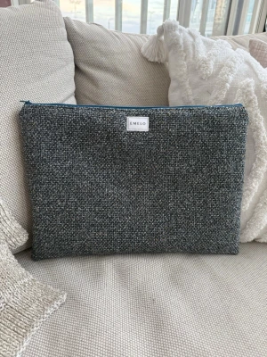 Blåmelerad datorväska från Emelo - Snygg och stilren datorväska från Emelo i blåmelerat, grovt vävt tyg. Väskan har en enkel rektangulär form och stängs med en blå dragkedja upptill. Perfekt för att skydda din laptop med en trendig look. Vadderat. Passar laptop med maxmått: 33x24cm