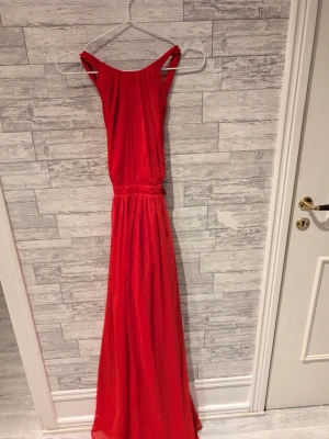 Röd långklänning med knyt i ryggen - Snygg röd långklänning med smala axelband och knytning i ryggen. Klänningen har en luftig och elegant passform, perfekt för sommarens alla tillfällen. Materialet känns lätt och följsamt.