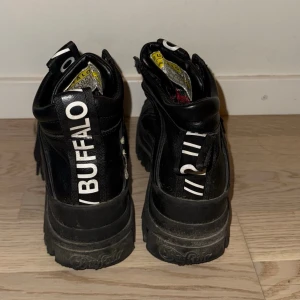 Svarta Buffalo kängor med chunky sula - Säljer ett par svarta Buffalo kängor med kraftig, chunky sula och högt skaft. Skorna har vita detaljer och logga på hälen samt tungan. Tillverkade i läderimitation med snörning framtill och cool streetwear-vibe.