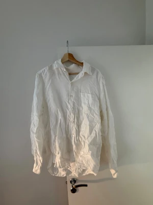 Vit linneskjorta från a days march - Klassisk vit skjorta i linne med lång ärm och knappar framtill. Skjortan har en bröstficka och avslappnad passform, perfekt för en stilren och enkel look. Materialet är luftigt linne som passar bra till varmare dagar.