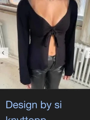 Svart långärmad knyttopp - Trendig svart långärmad topp från Design by Si med djup v-ringning och snygg knytning framtill. Toppen är croppad och har en figurnära passform som framhäver midjan. Perfekt att styla med höga byxor för en cool look.