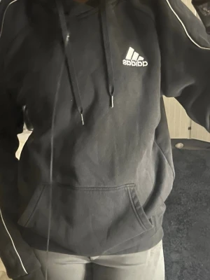 Svart hoodie från Adidas - Svart hoodie från Adidas med vit logga på bröstet och vita ränder längs ärmarna. Pris kan diskuteras!