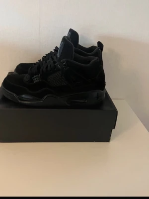 Svarta Air Jordan 4 Retro sneakers - Snygga helsvarta Air Jordan 4 Retro sneakers med klassisk siluett och coola detaljer. Skorna har meshpaneler, mockaliknande material och ikoniska Jumpman-loggor på plösen. Perfekta för dig som gillar streetwear och vill sticka ut  stilrena kicks.