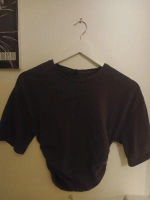 Svart t-shirt från Gina Tricot - En basic Mörk grå t-shirt från Gina Tricot med rund halsringning och korta ärmar.Har scrunch på båda sidorna så den har en snygg detalj💛Tillverkad i mjuk bomull som känns skön mot huden. Perfekt att matcha med jeans eller kjol för en enkel och clean look. Skriv om ni vill ha bild på🙌